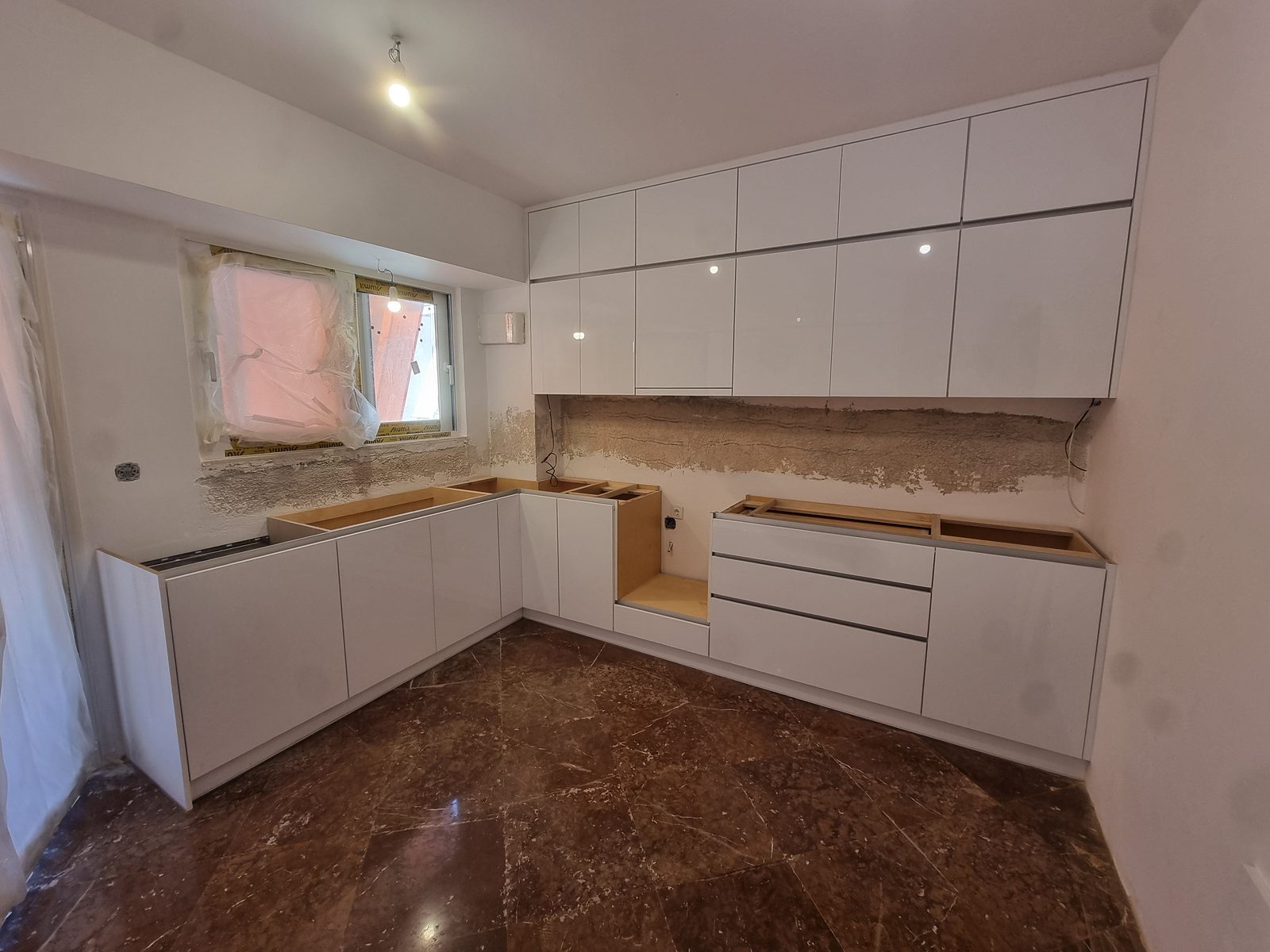 Λευκή High Gloss κουζίνα σε διάταξη Γ, με κρεμαστά ντουλάπια μέχρι το ταβάνι, κατά την τοποθέτηση