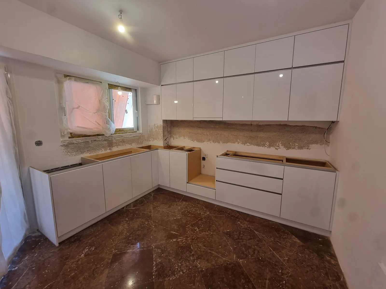 Λευκή High Gloss κουζίνα σε διάταξη Γ, με κρεμαστά ντουλάπια μέχρι το ταβάνι, κατά την τοποθέτηση
